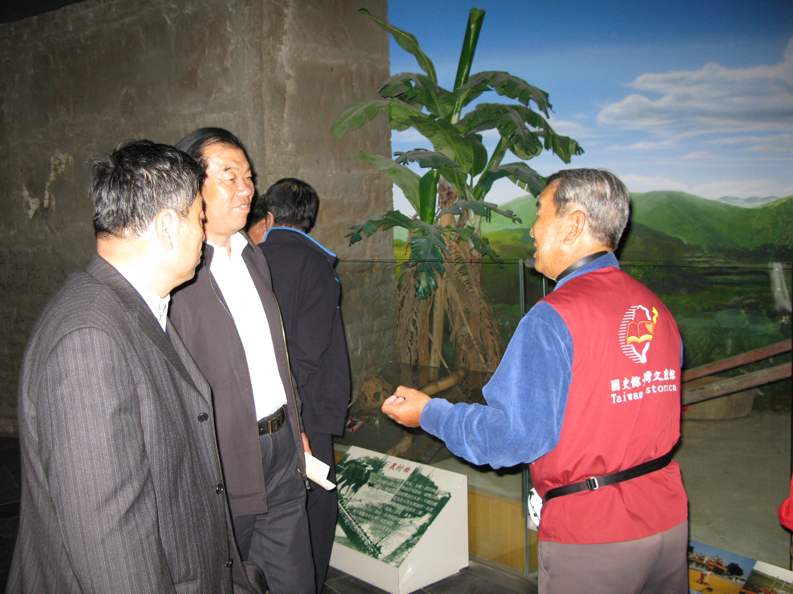 本館志工簡吉政老師(右1)親切地為來賓導覽展示文物